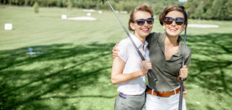 Portrait of a two female friends standing with golf clubs on a golg course
